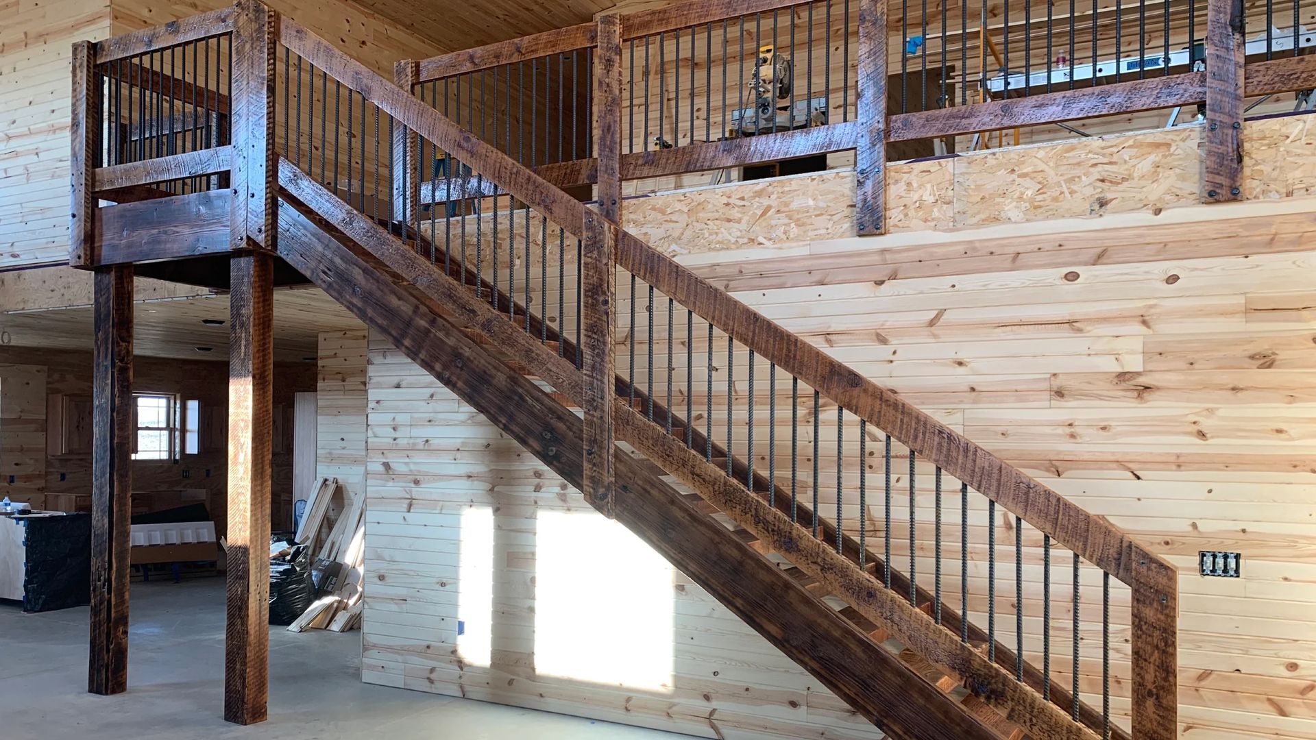 Wooden staircase with black metal balusters in a building with wood paneling.