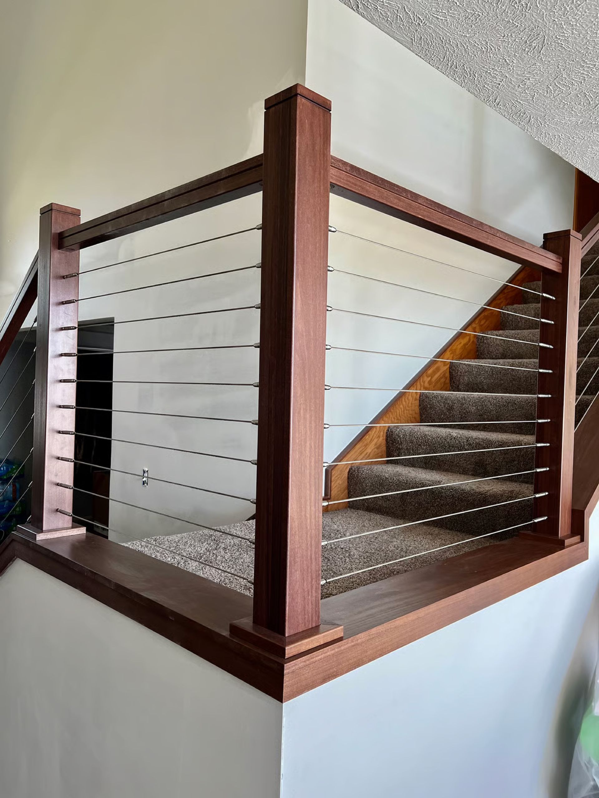 Wooden staircase with cable railing, brown carpet steps, and white walls.