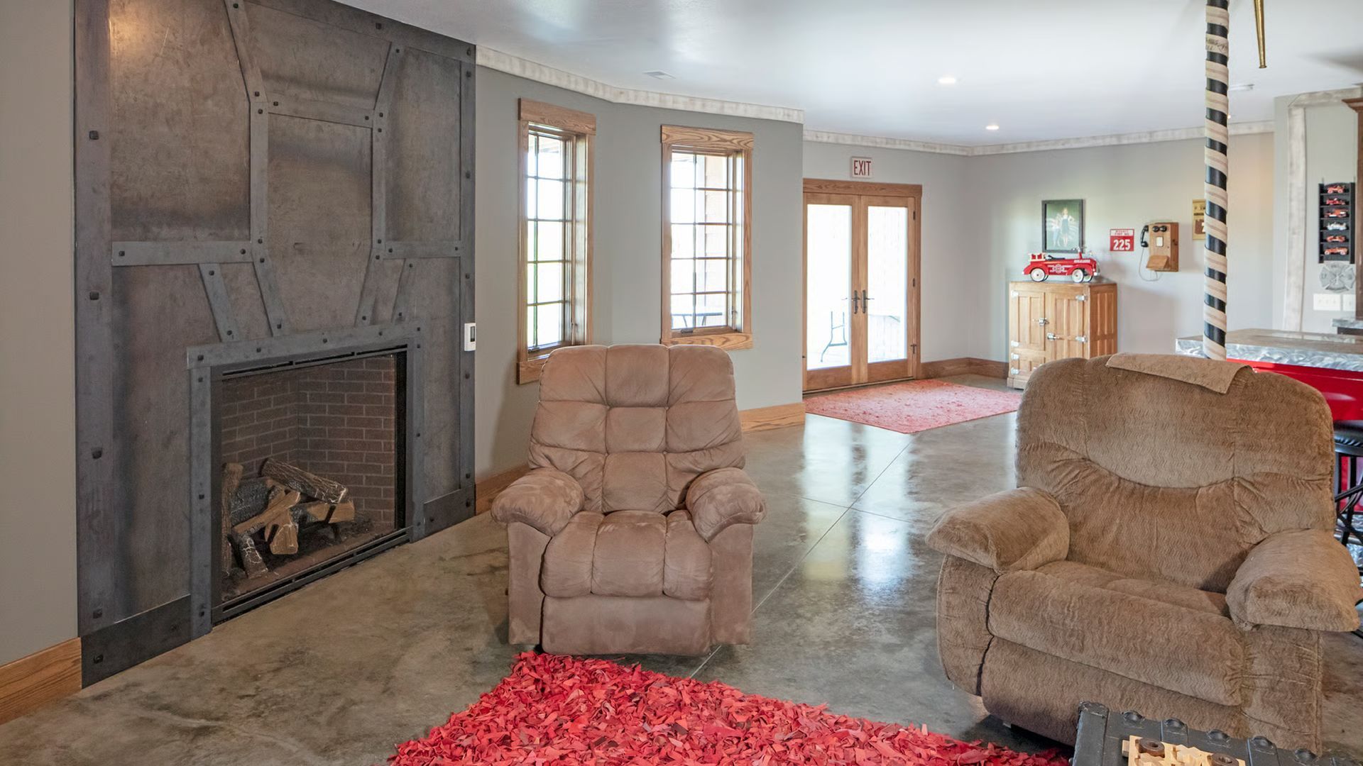 Living room with industrial fireplace, two brown recliners, and a red rug on a concrete floor.