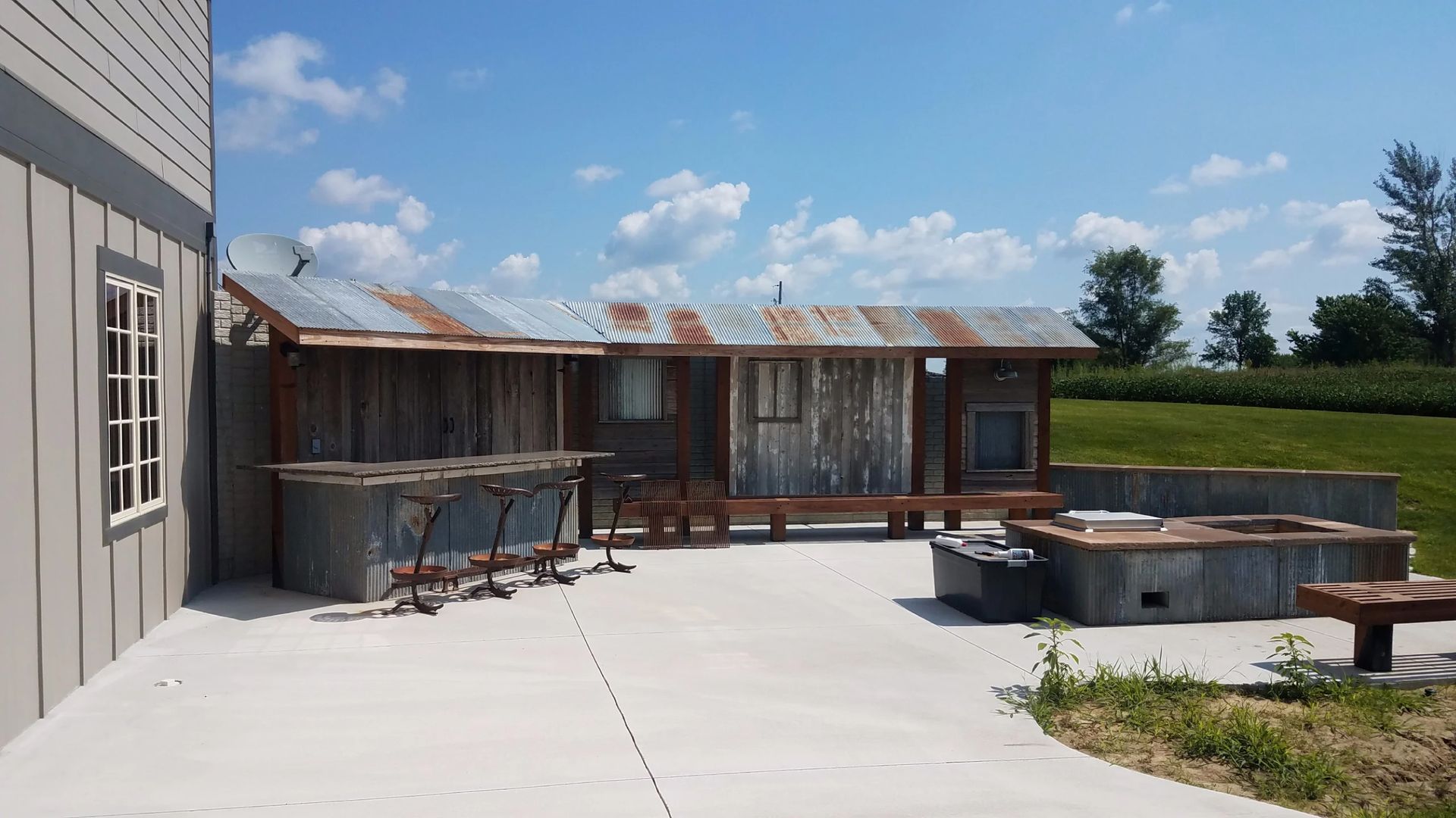A rustic outdoor bar and seating area with a tin roof under a bright blue sky.