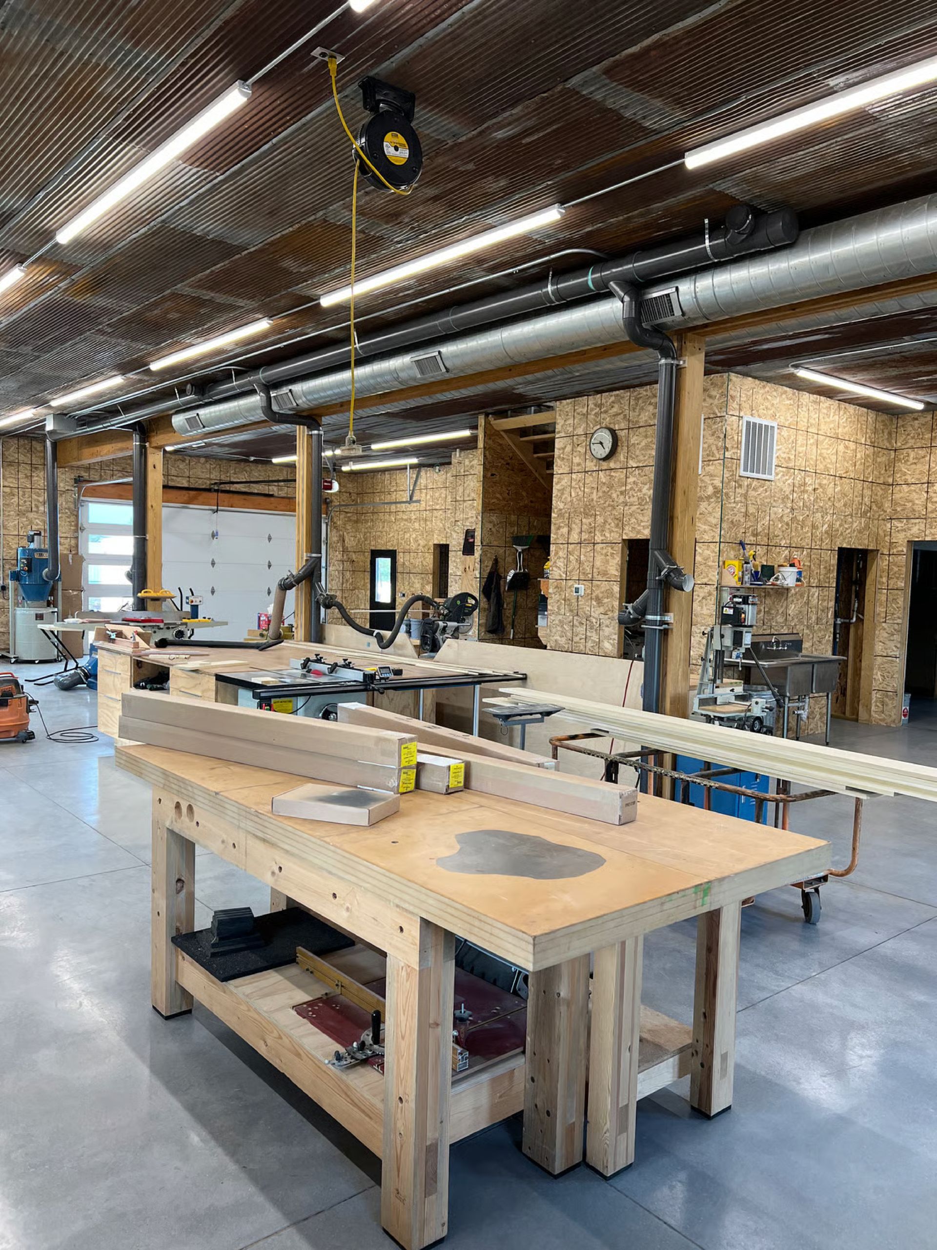 Woodworking shop interior with workbenches, tools, and ventilation system.