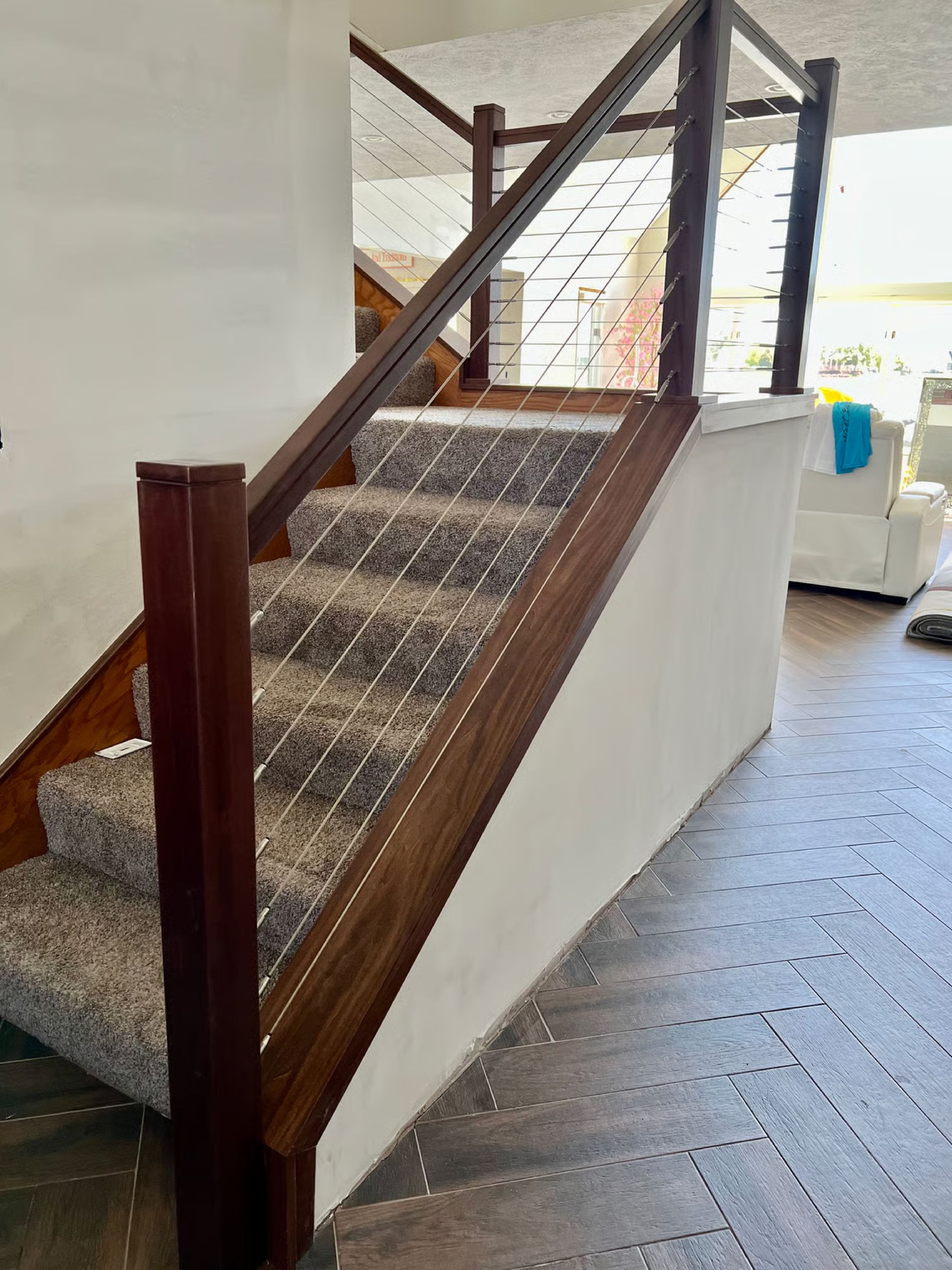 Staircase with brown wooden railing, carpeted steps, and white wall. Floor is tiled.