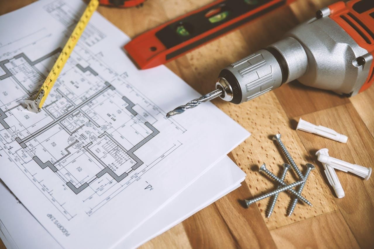 Table with a floor plan, drill, screws, and a tape measure