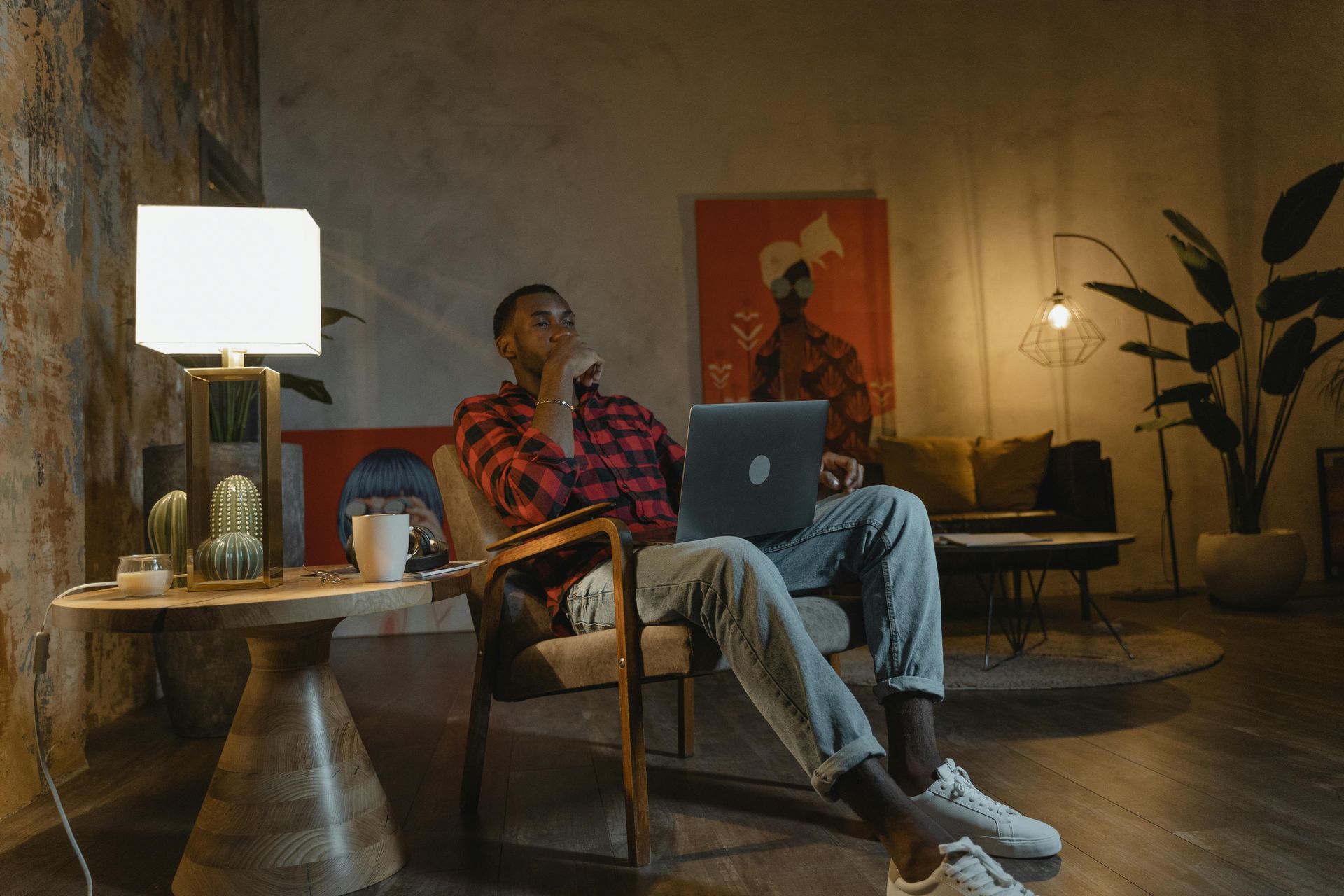 A man works on a laptop in a warmly lit remodeled basement.