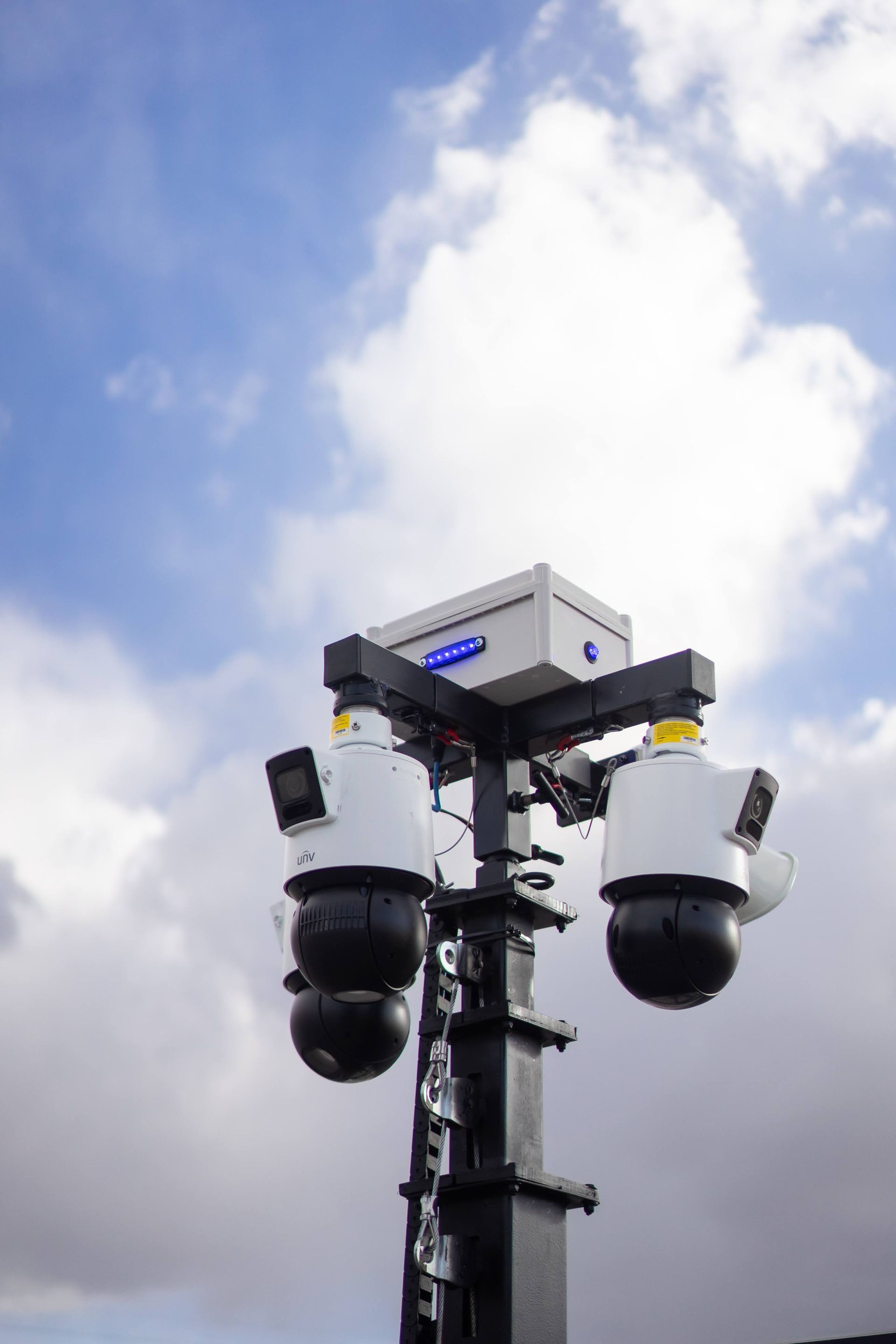 A man wearing a security shirt is standing in front of a blue light.