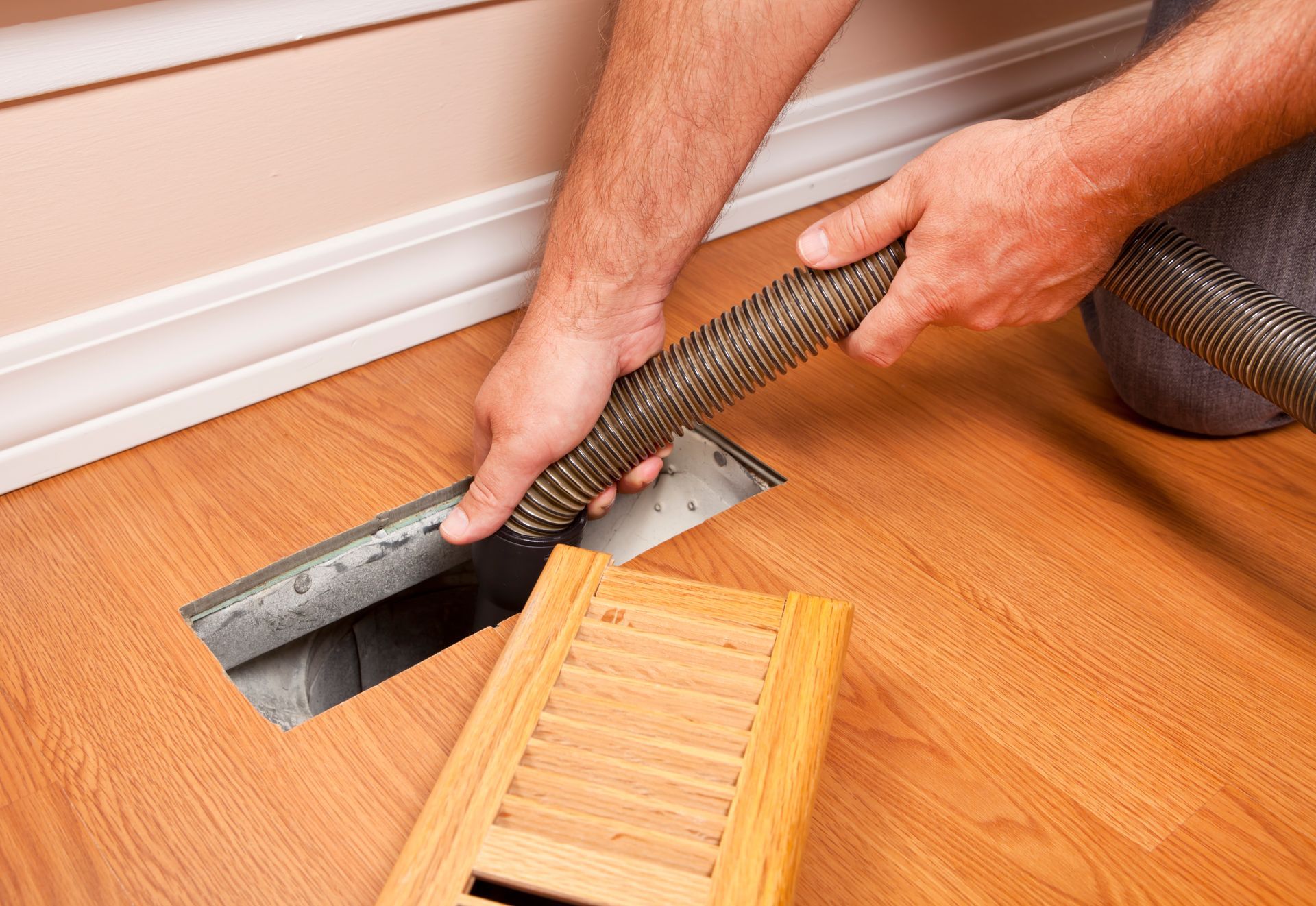 A man is using a vacuum cleaner to clean a vent on the floor.