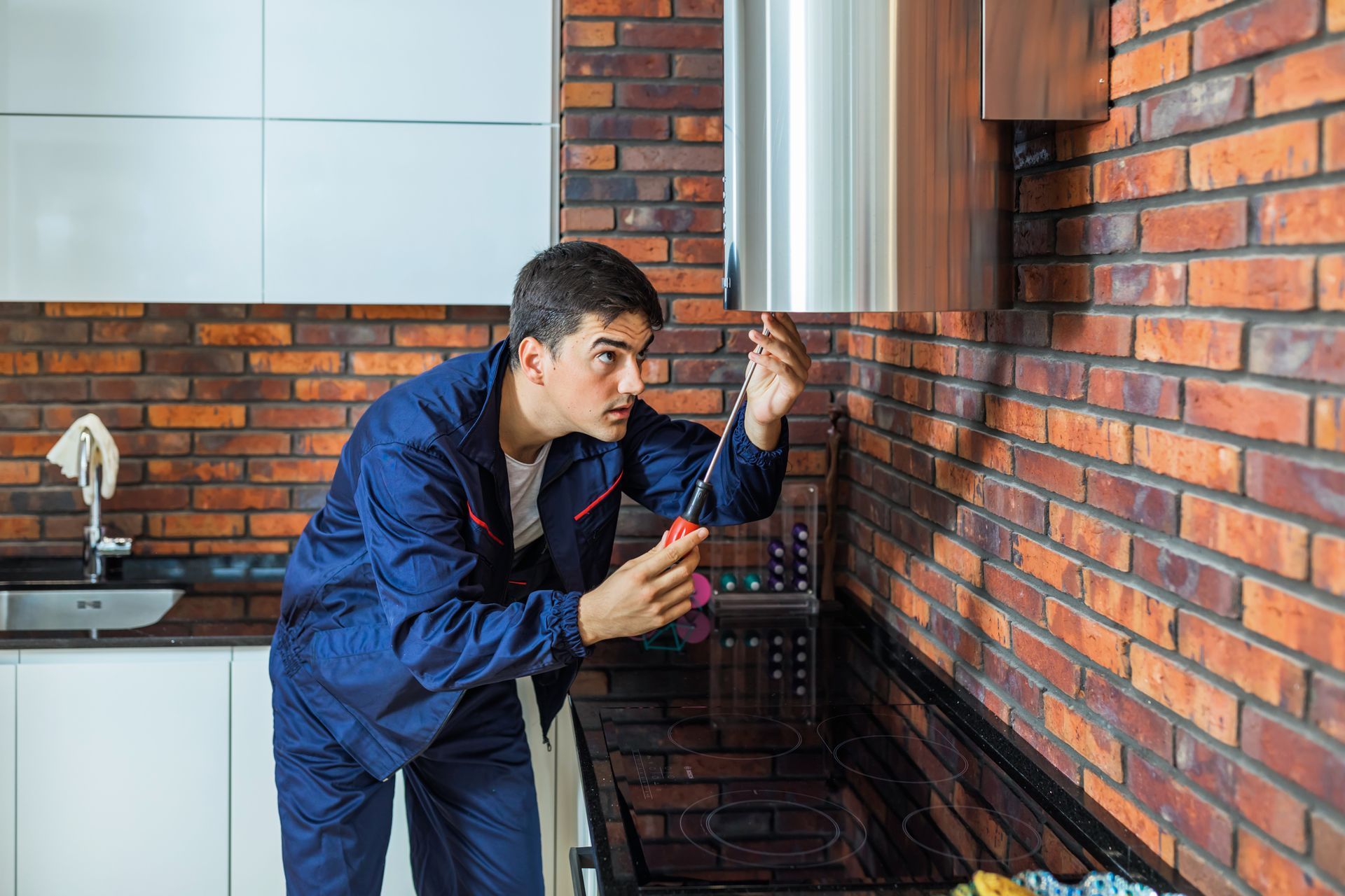A man is cleaning a duct in a kitchen with a screwdriver.