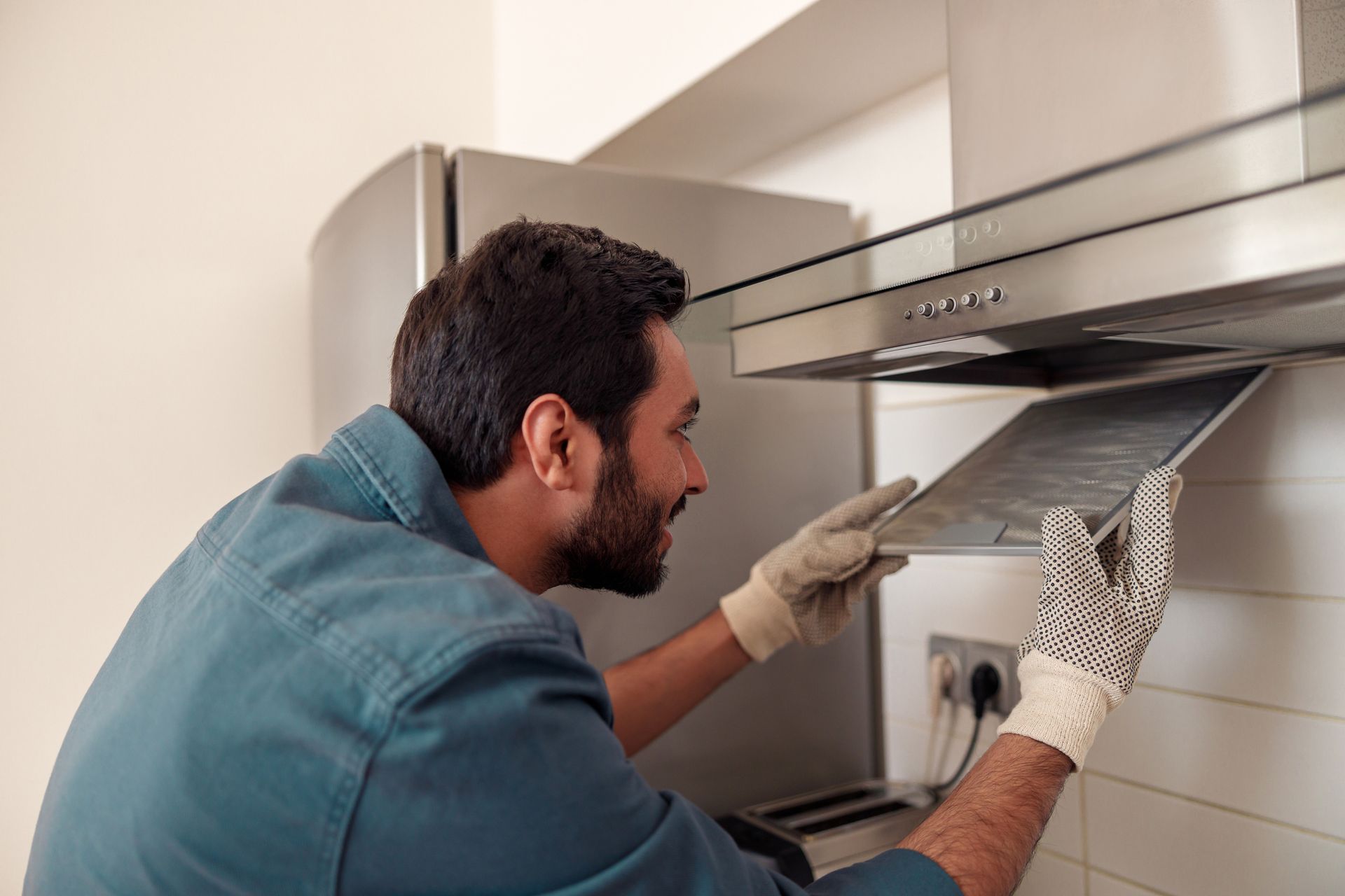 A man is cleaning the Exhaust fan in a kitchen.