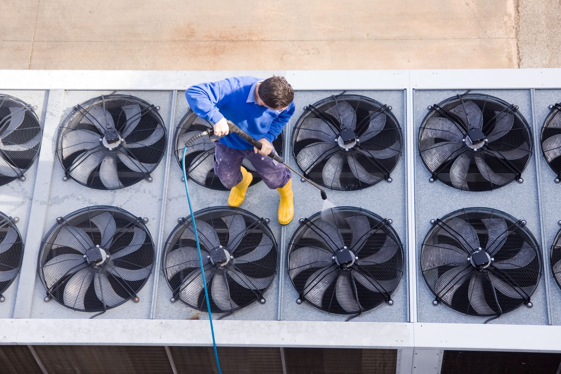 A man is cleaning the fans on the roof of a building.