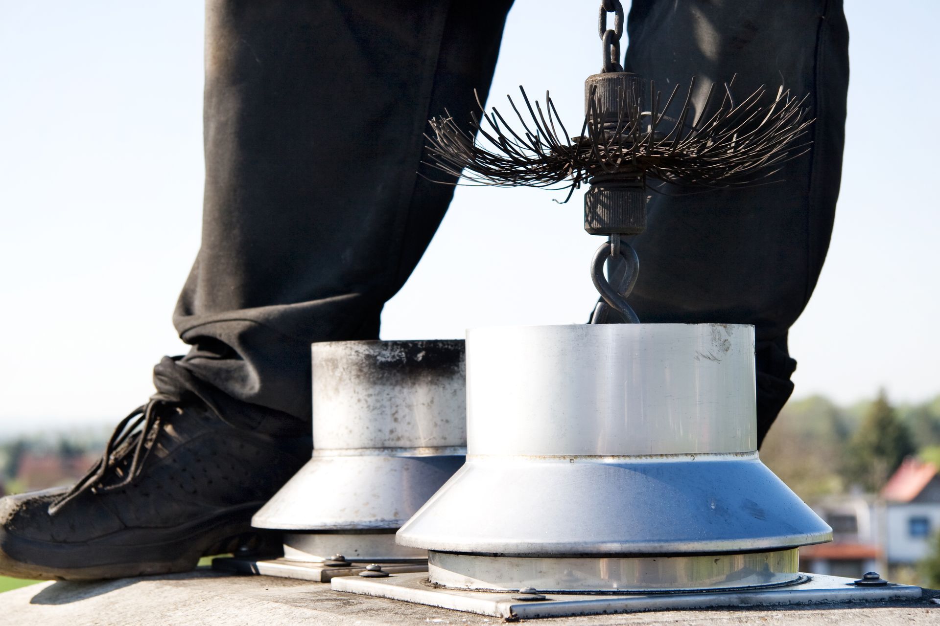 A person is standing on a roof with a chimney brush