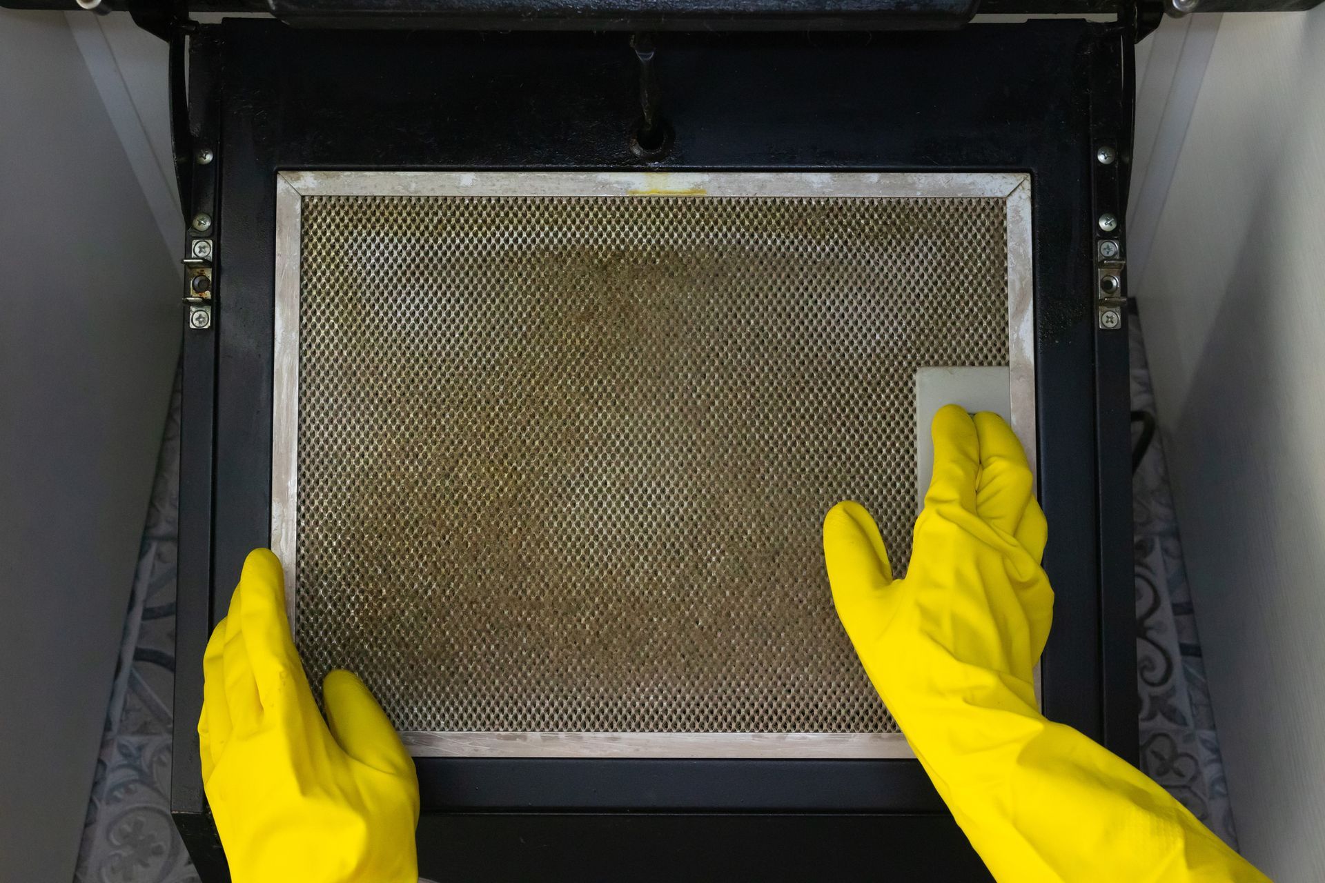 A person wearing yellow gloves is cleaning a dirty oven door.