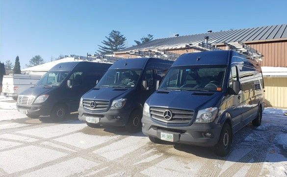 Three blue vans are parked in front of a building in the snow.
