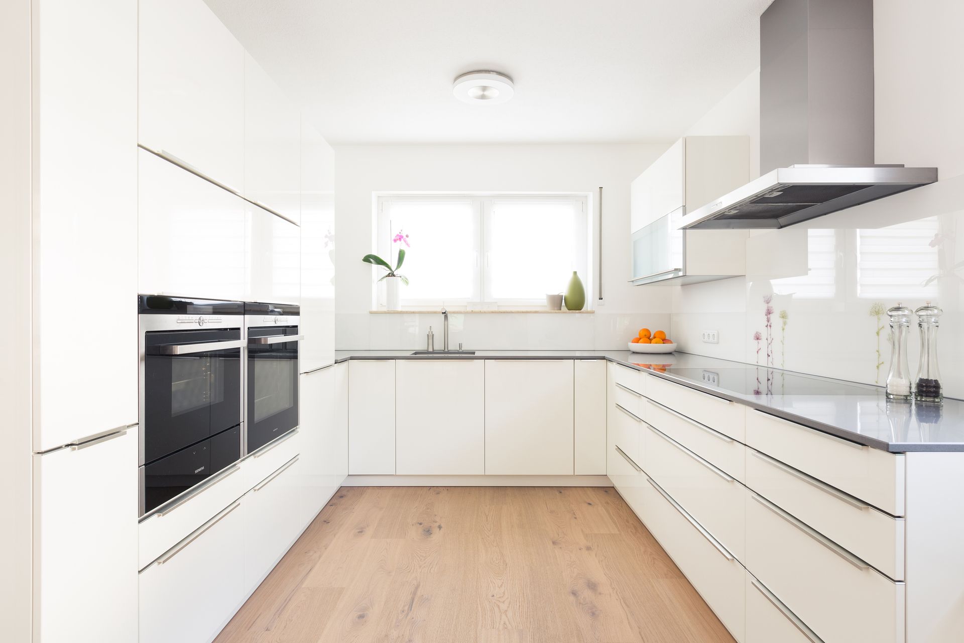 A kitchen with white cabinets and black appliances and a wooden floor.