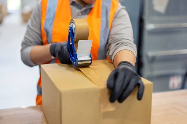 A person is taping a cardboard box in a warehouse. - Port Saint John, FL - Shipping Depot of Port St John