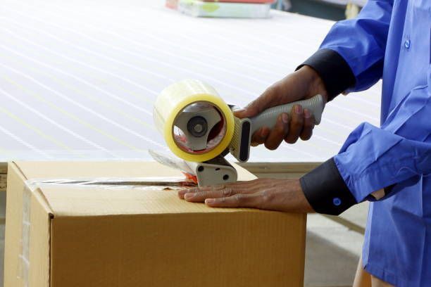 A person is using a tape dispenser to tape a box. - Port Saint John, FL - Shipping Depot of Port St John