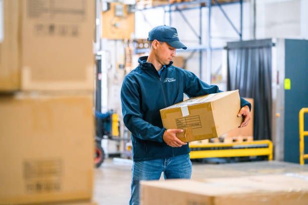 A man is holding a cardboard box in a warehouse. - Port Saint John, FL - Shipping Depot of Port St John
