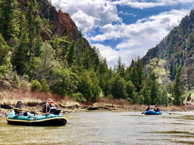 A group of people are rafting down a river with mountains in the background.