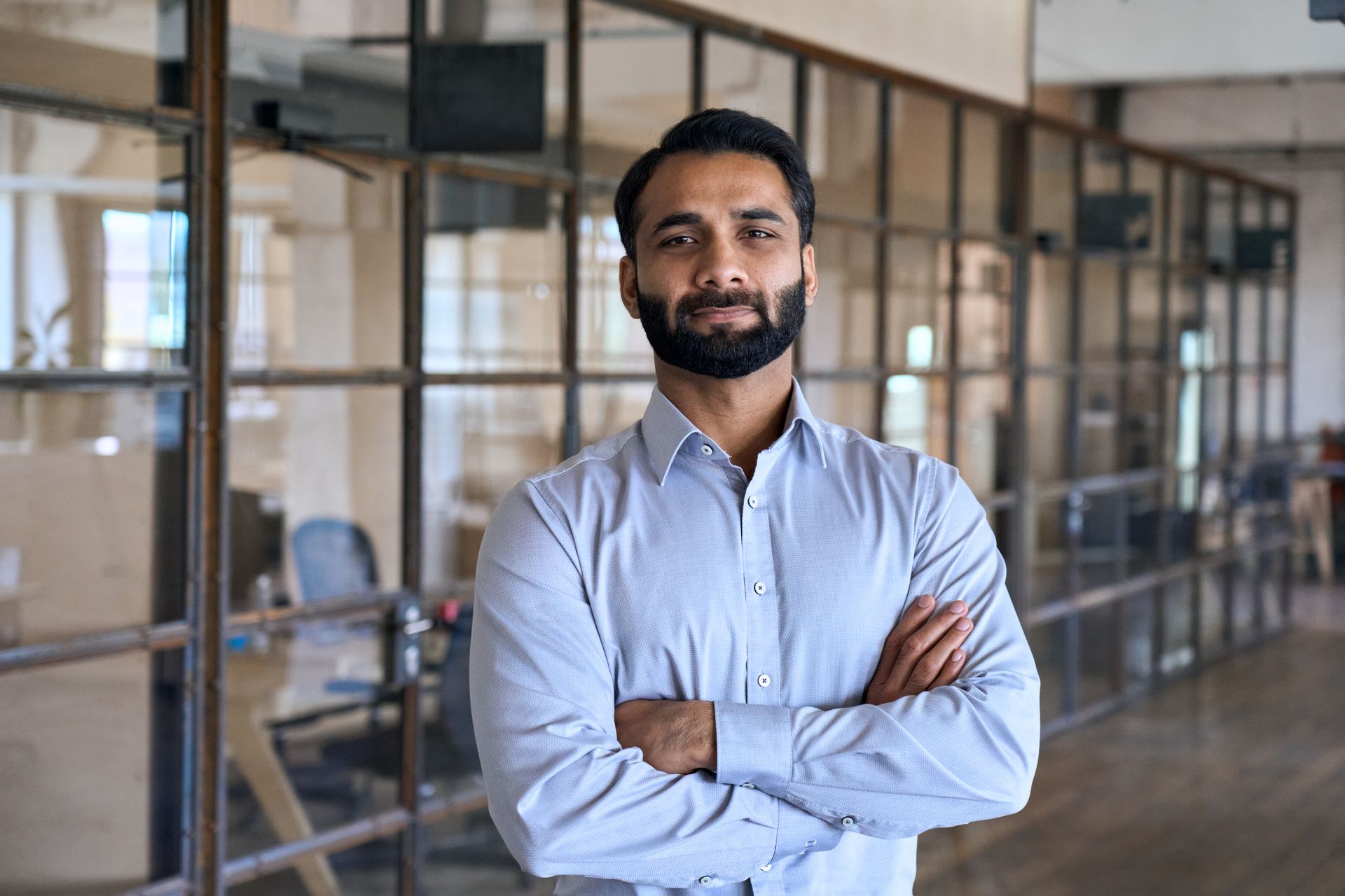 A man with a beard is standing in an office with his arms crossed.