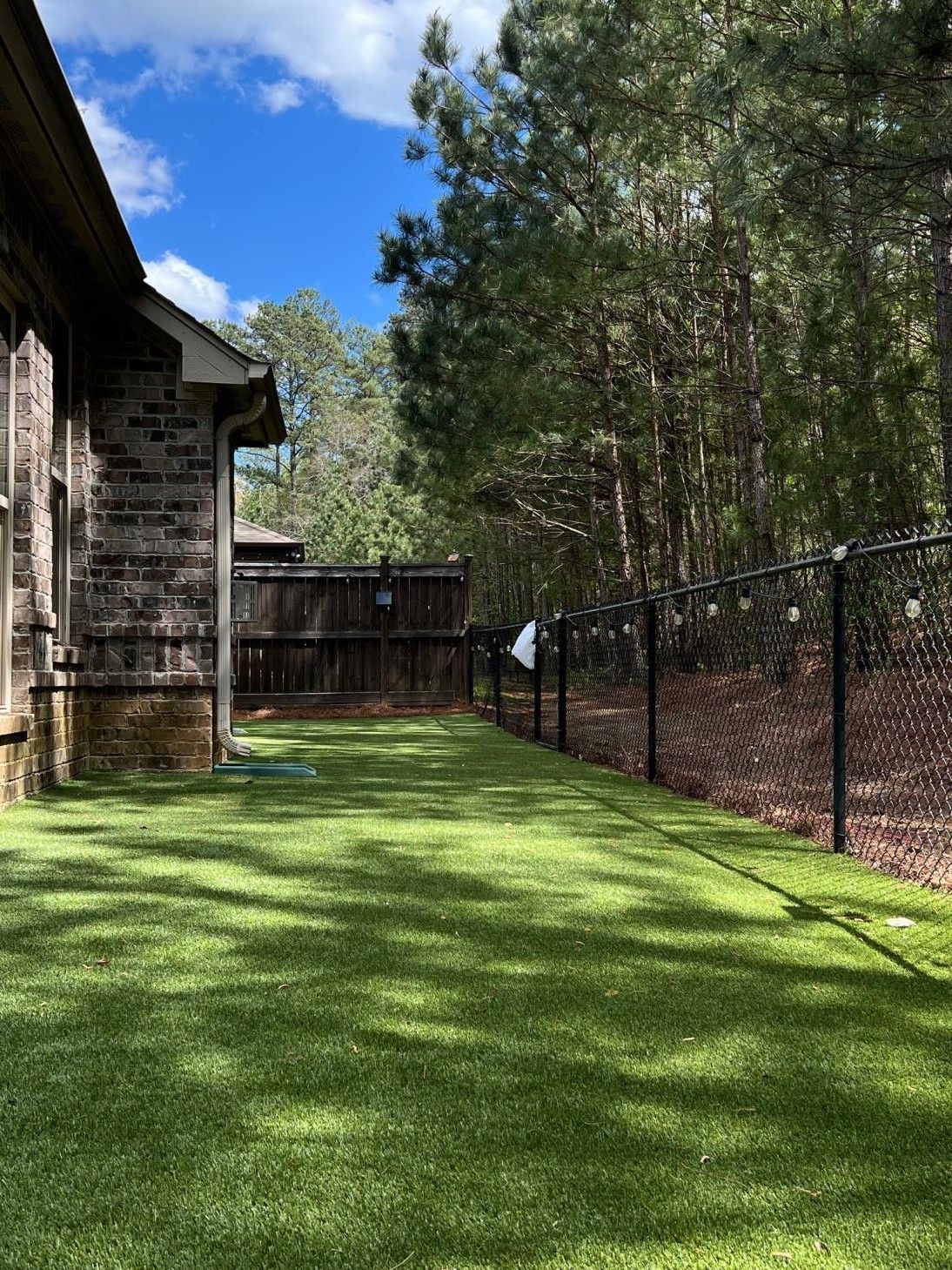 A fenced in yard with a lush green lawn and trees in the background.