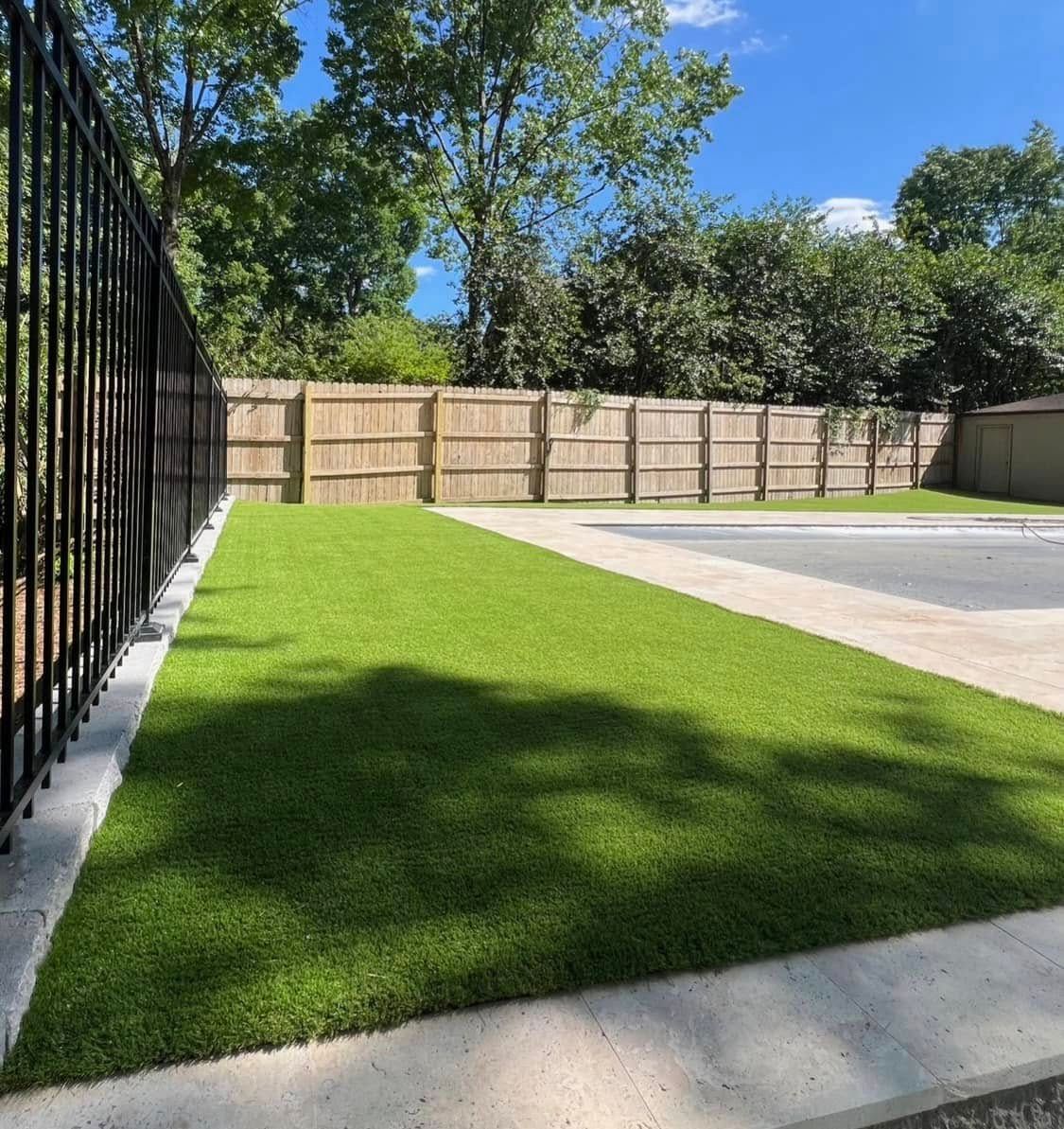 A backyard with a fence and a lush green lawn