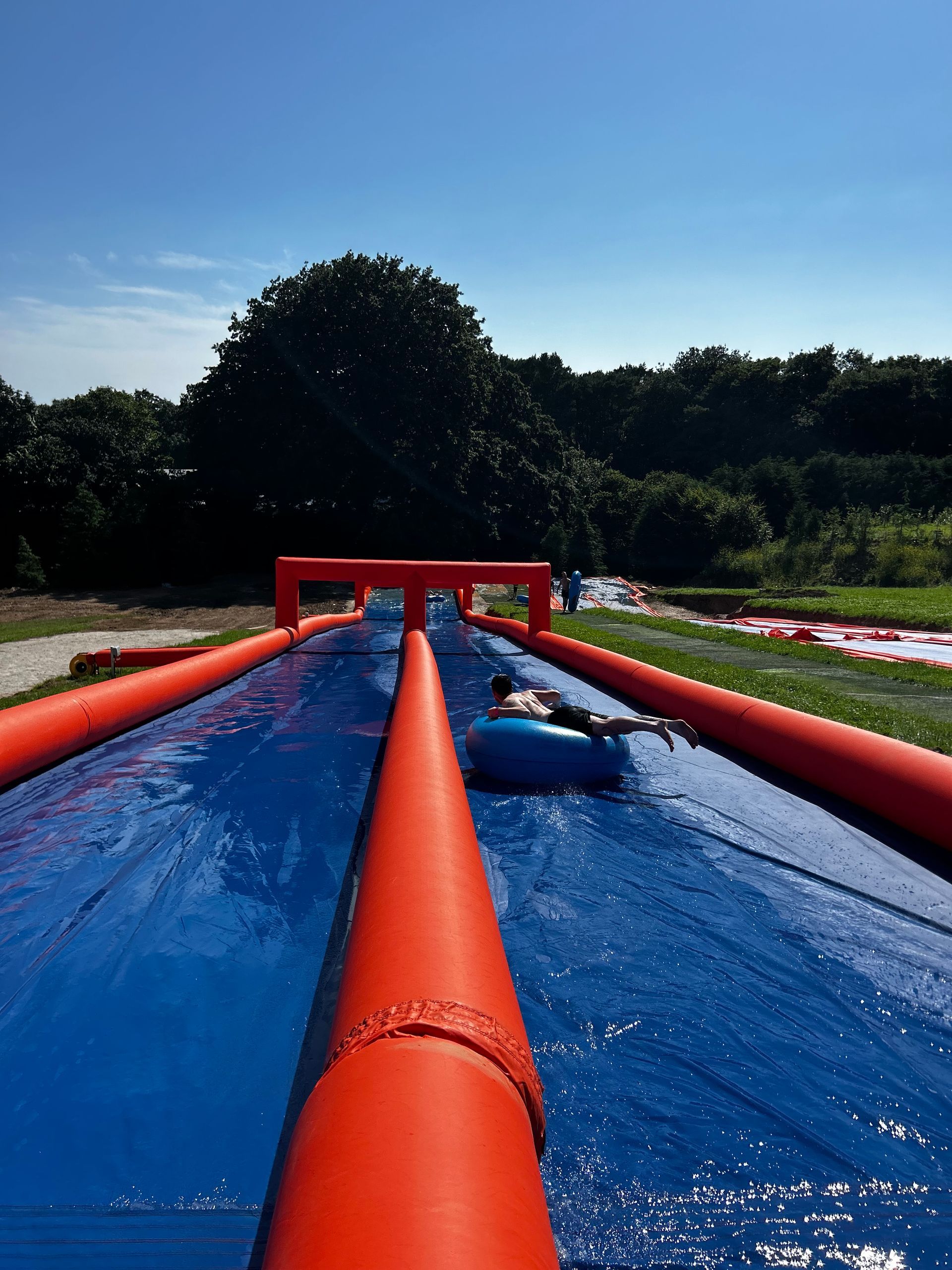A person slides down a blue water slide with vibrant orange inflatable barriers on a sunny day.