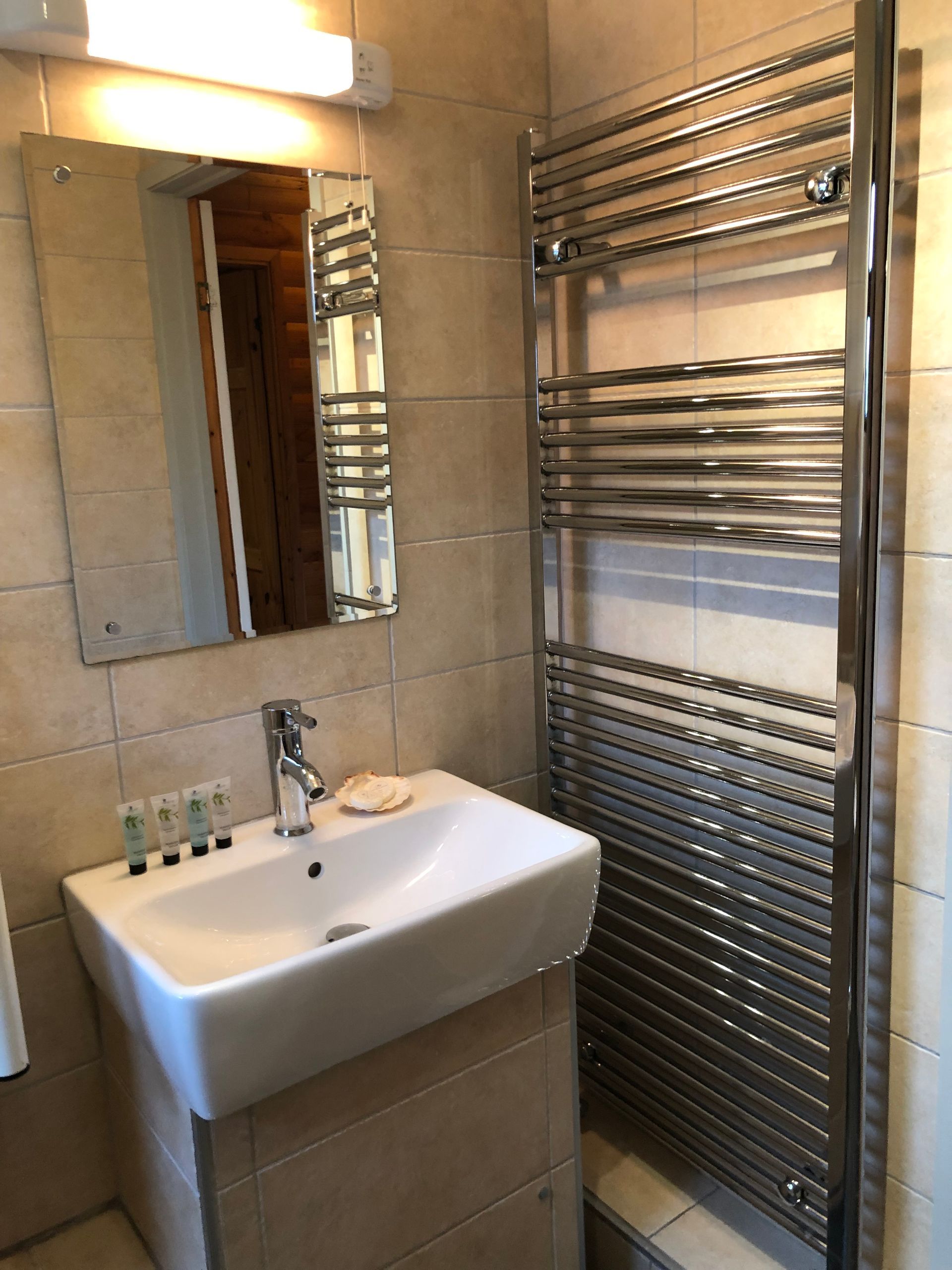 A modern bathroom with a rectangular wall-mounted sink, a mirror, and a tall, polished chrome ladder-style towel radiator.