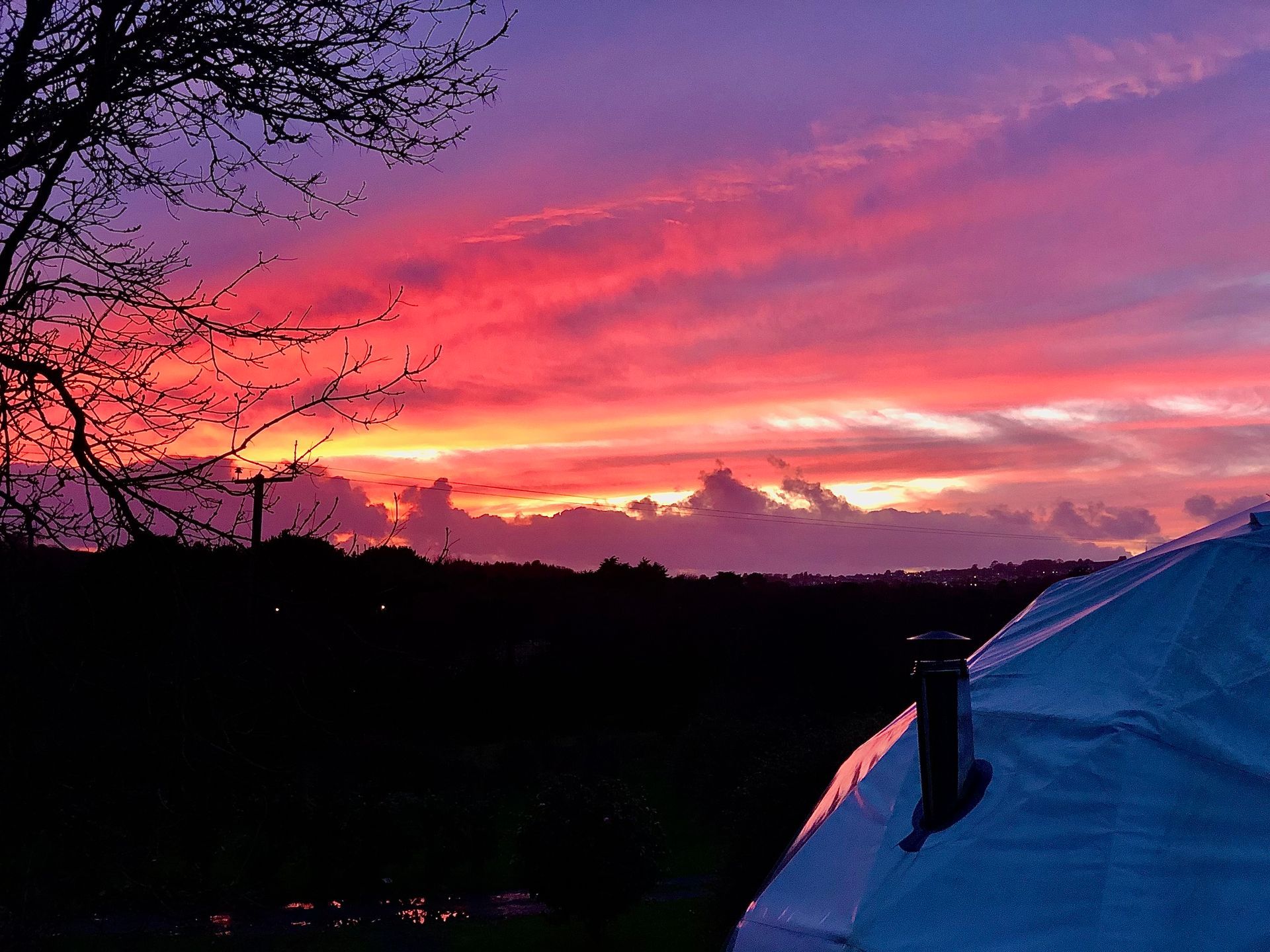 A vibrant sunset with streaks of red, orange, and purple light illuminating clouds above a dark, silhouetted landscape.