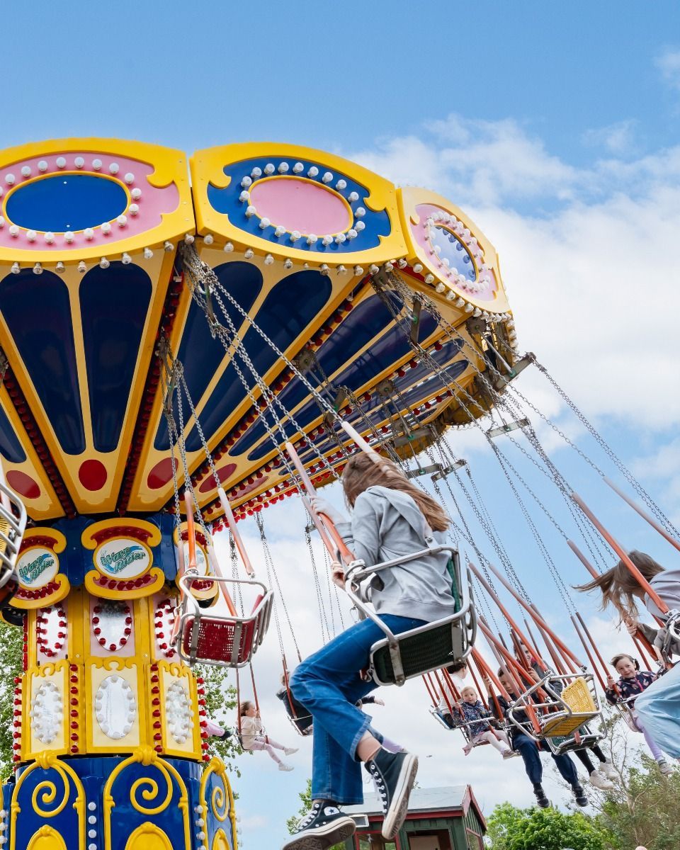 People riding a tall, colorful swing carousel against a bright blue sky.
