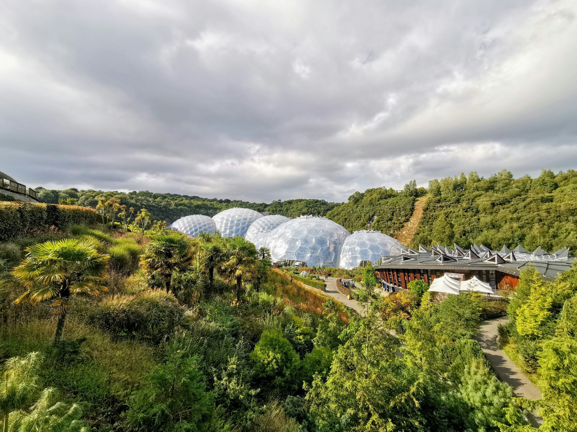 The Eden Project's iconic geodesic domes nestled in a lush, green landscaped quarry under a cloudy sky.