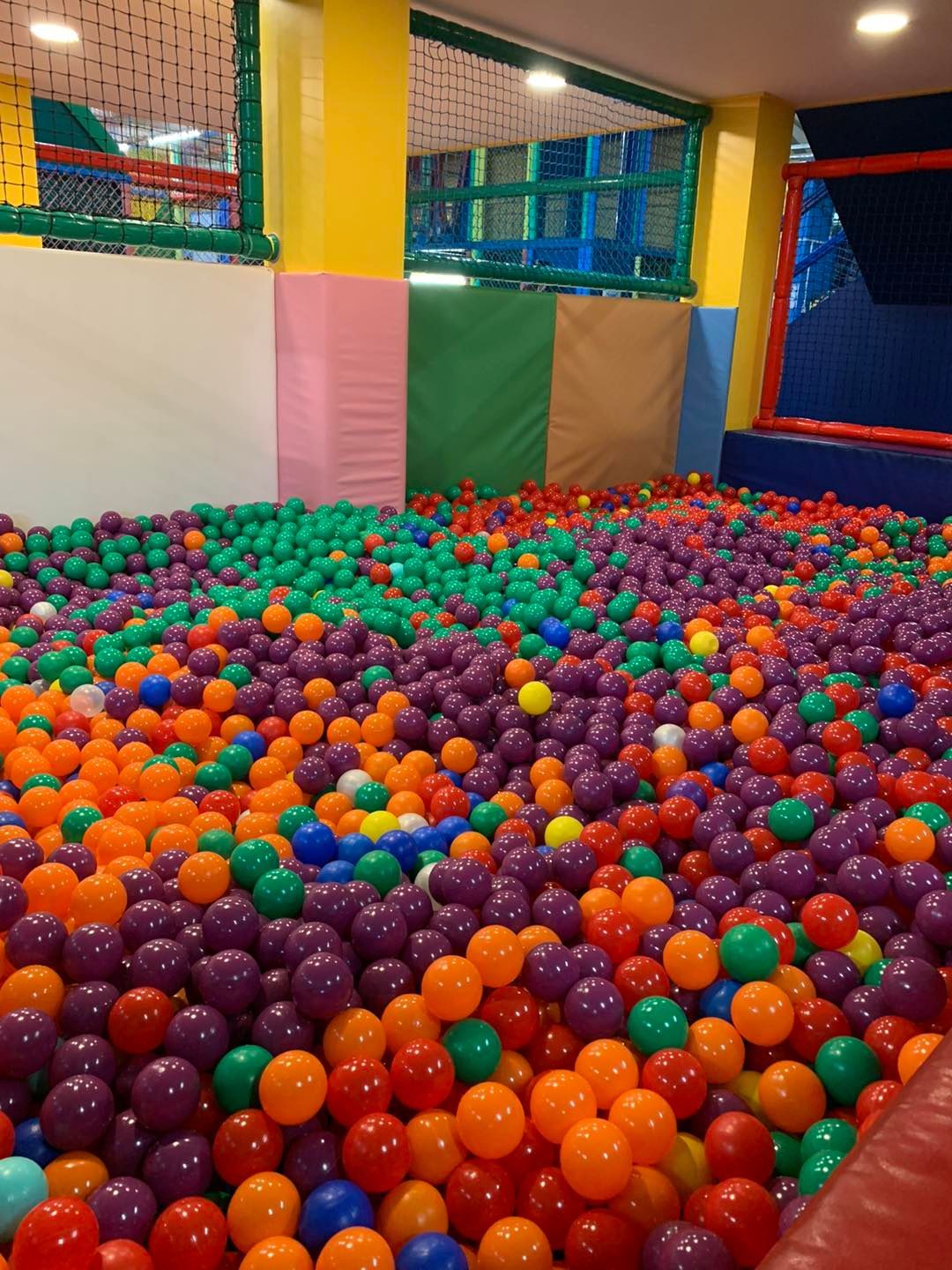 A ball pit filled with many colorful plastic balls, set inside an indoor playground area with padded walls.