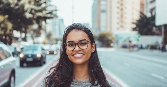 Eine Frau mit Brille steht lächelt auf einer Stadtstraße.