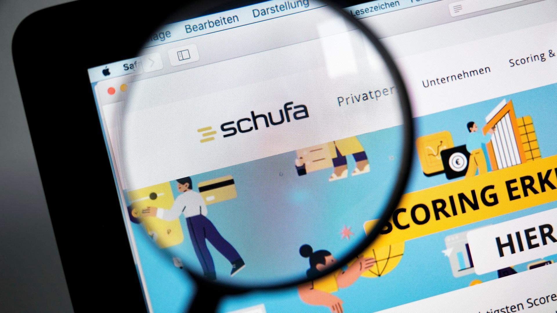 Zum Betrachten eines Computerbildschirms wird eine Lupe verwendet. Schufa-Logo.