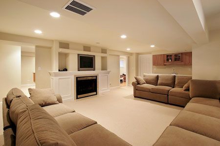 Spacious beige basement living room with two sofas, fireplace, recessed lighting, and wall-mounted TV.