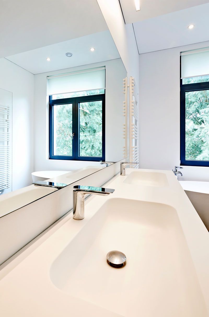 Bright modern bathroom with a white sink, mirror, and two blue-framed windows.