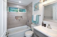Modern bathroom with bathtub, toilet, vanity sink, mirror, and gray tile walls