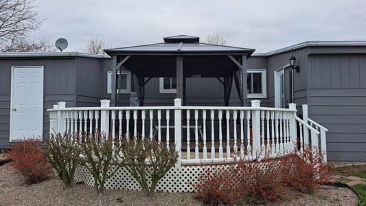 Front porch of a gray house with white railing, screened entry, and leafless shrubs in front