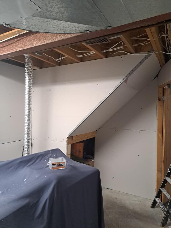 Partially finished basement with slanted drywall, exposed ceiling joists, and a covered item in the foreground