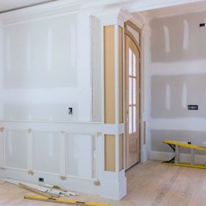 Partially finished room with white drywall, paneled walls, arched doorway, and construction tools on the floor
