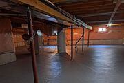 Empty basement with exposed beams, support posts, and concrete floor under low ceiling.