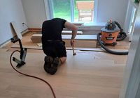 Person kneeling on a hardwood floor, sanding boards during a room renovation, with a vacuum nearby
