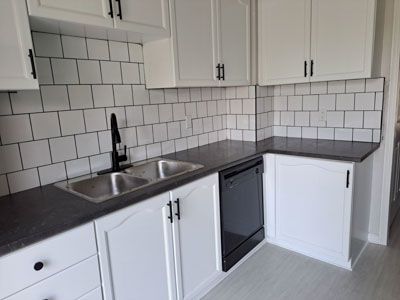 Modern white kitchen with gray countertops, subway tile backsplash, sink, dishwasher, and cabinets