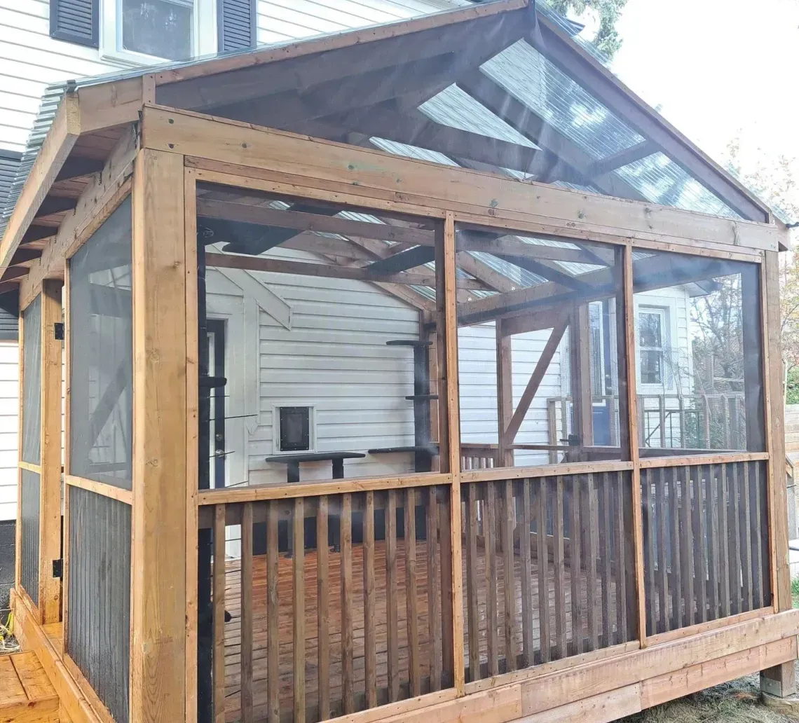 Wooden screened porch with a gabled roof attached to a house, framed in unfinished lumber.