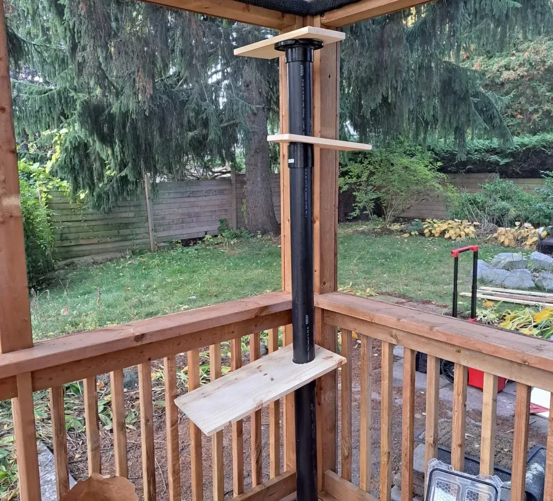 Wooden backyard porch with railing, bird feeder pole, and garden view beyond the screen enclosure