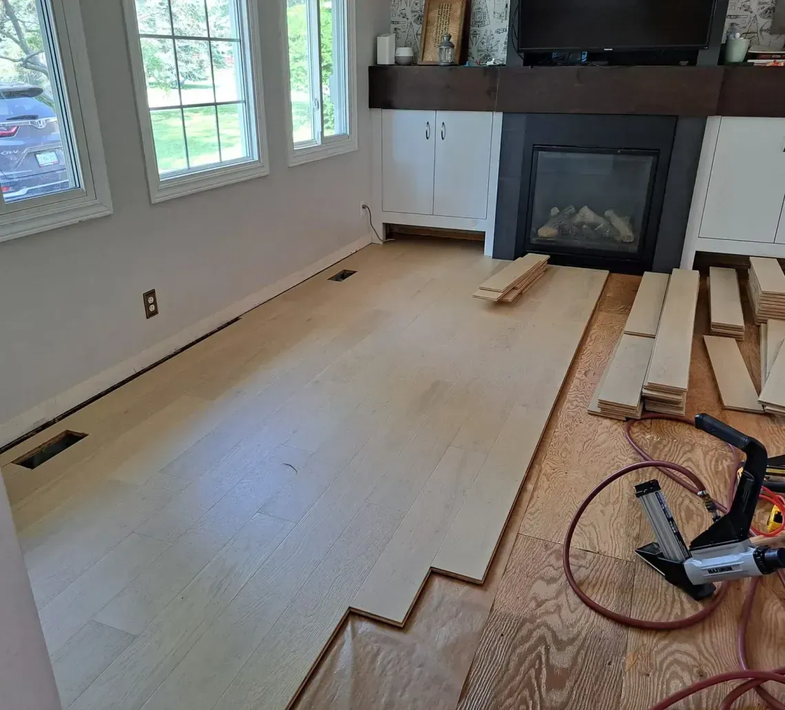 Partially finished living room with new hardwood floor, fireplace, windows, and stacked wood; bicycle in foreground