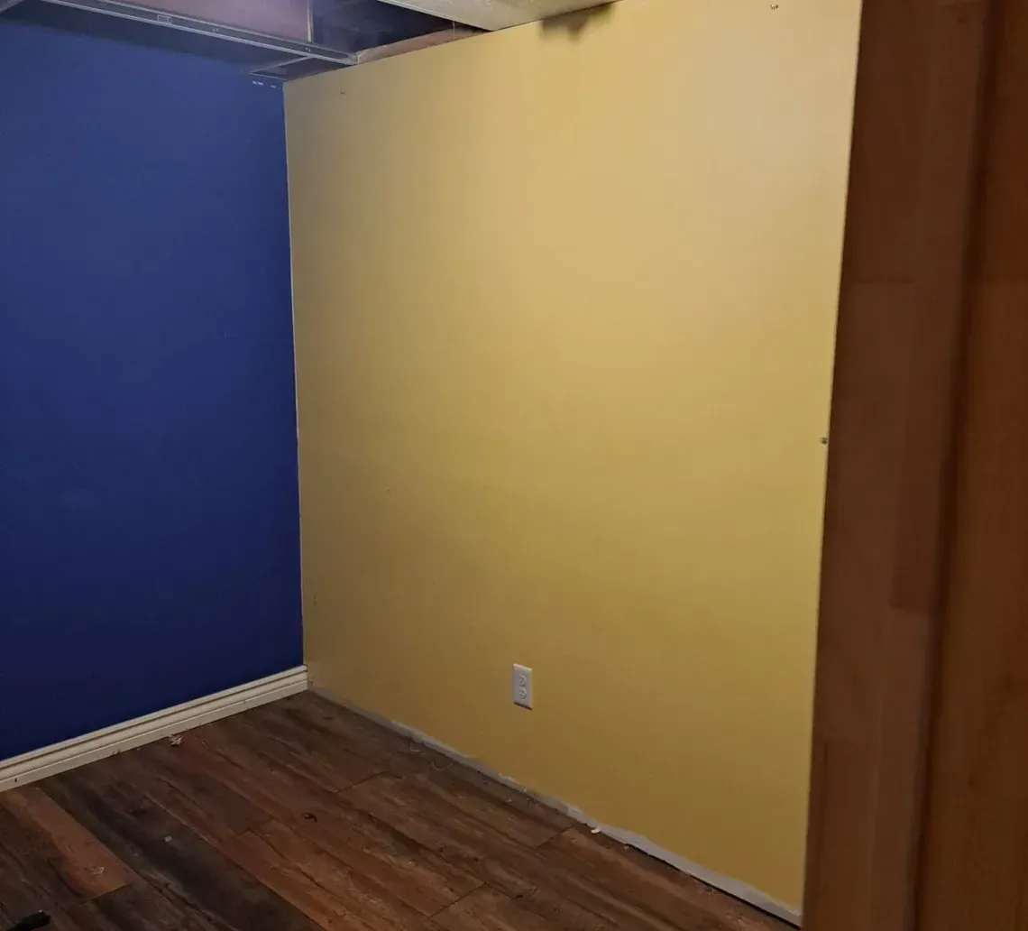 Empty room with blue and yellow walls, wood floor, and exposed ceiling.