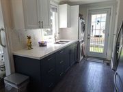Modern kitchen galley with dark cabinets, white countertops, and a glass back door letting in light.