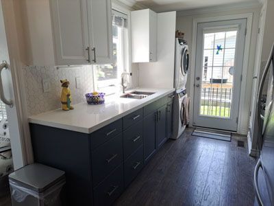Modern kitchen galley with dark cabinets, white countertops, and a glass back door letting in light.