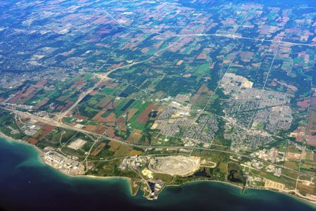 Aerial view of land meeting a body of water, featuring a quarry, farmlands, and a suburban area.
