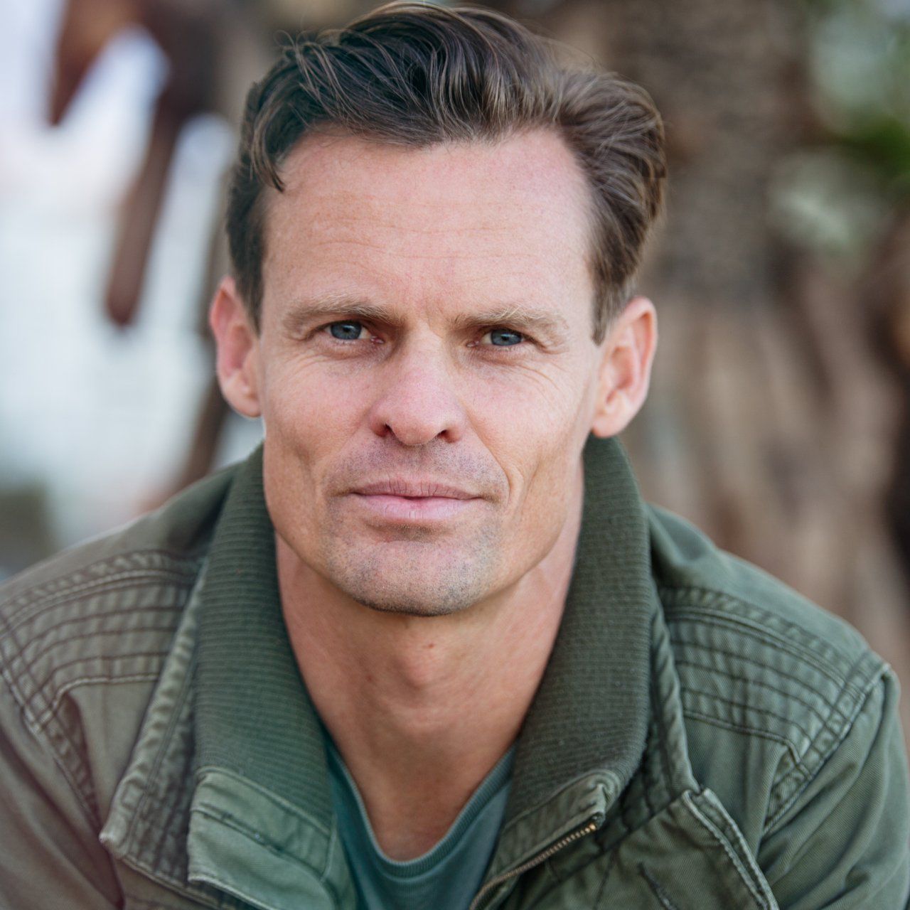 A man in a green jacket is looking at the camera