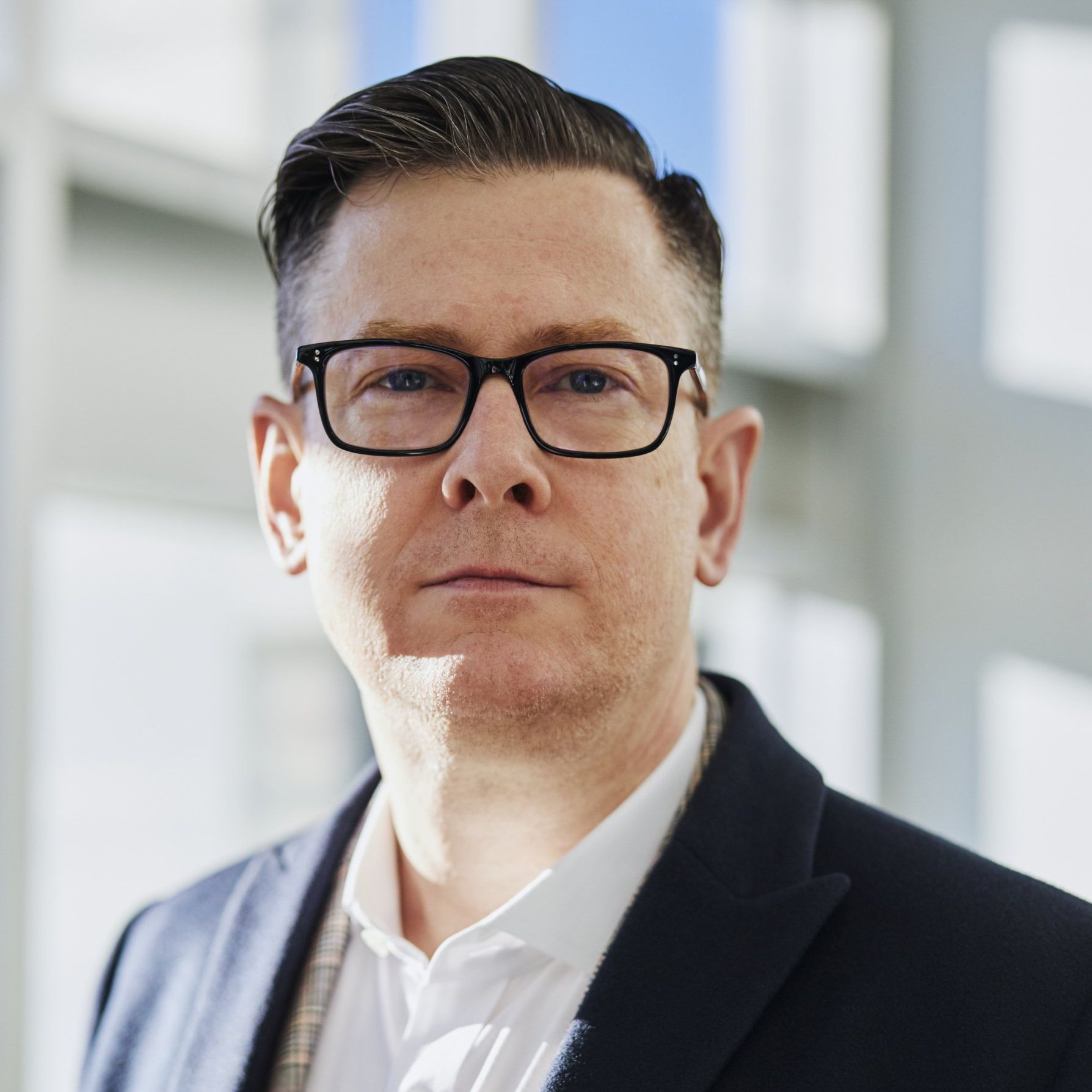 A man wearing glasses and a suit looks at the camera